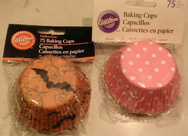 Cupcake liners with designs on the outside: on the left, an orange Halloween liner with a black bat, and on the right, a pink liner with white polka-dots.