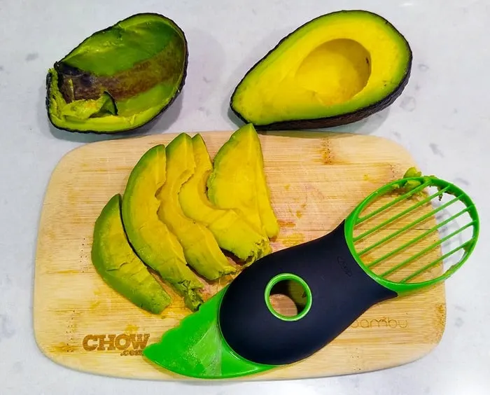 slices of avocado on a small cutting board with an avocado slicer