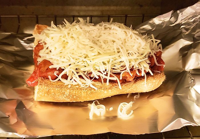 Tomato parm sandwich with shredded cheese on top on aluminum foil in a toaster oven