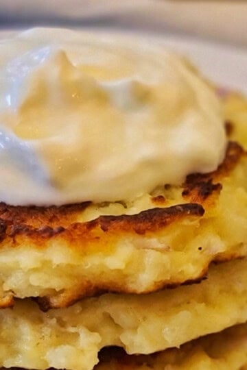 A stack of potato pancakes with sour cream on top.