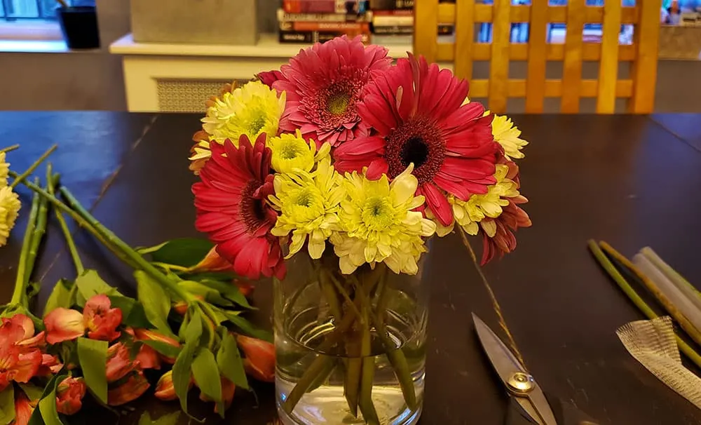 A vase of red and yellow flowers surrounded by flower arranging supplies.