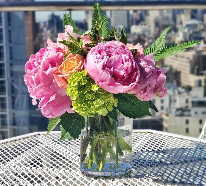 A vase of flowers on an outside table in front of a blurry view of Manhattan