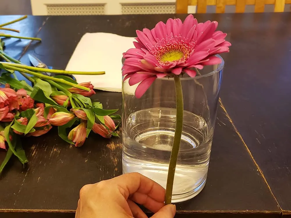 One pink flower in front of a vase.