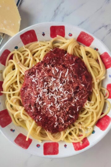 A bowl of spaghetti with red sauce and a sprinkling of shredded parmesan cheese.