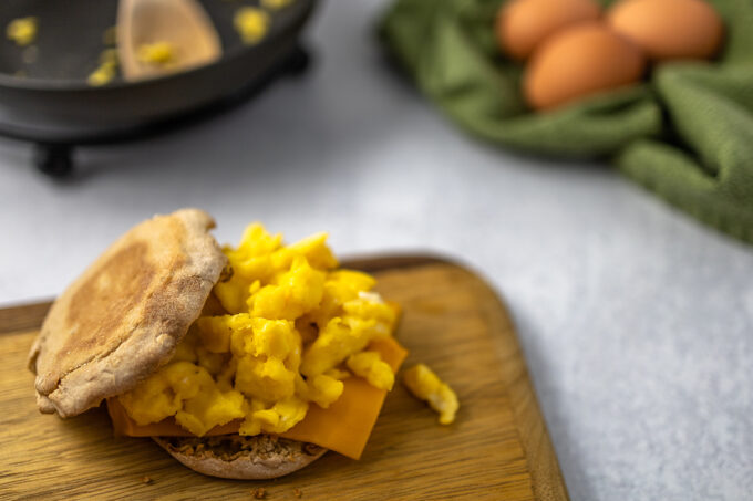 A wheat English muffin with scrambled eggs on top of yellow cheese.