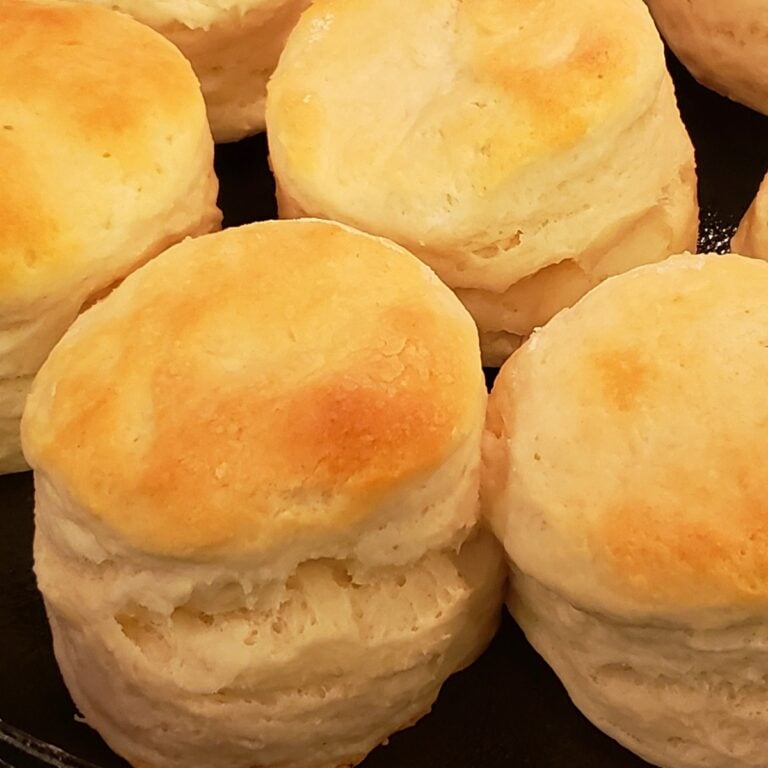 Tall fluffy biscuits with golden tops, in a cast iron pan.