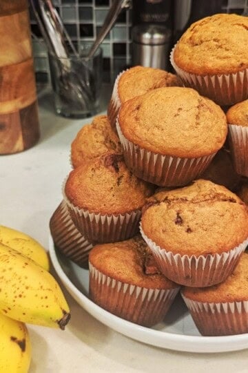Reese's Peanut Butter Cup Banana Muffins piled on a plate, next to a bunch of ripe bananas.