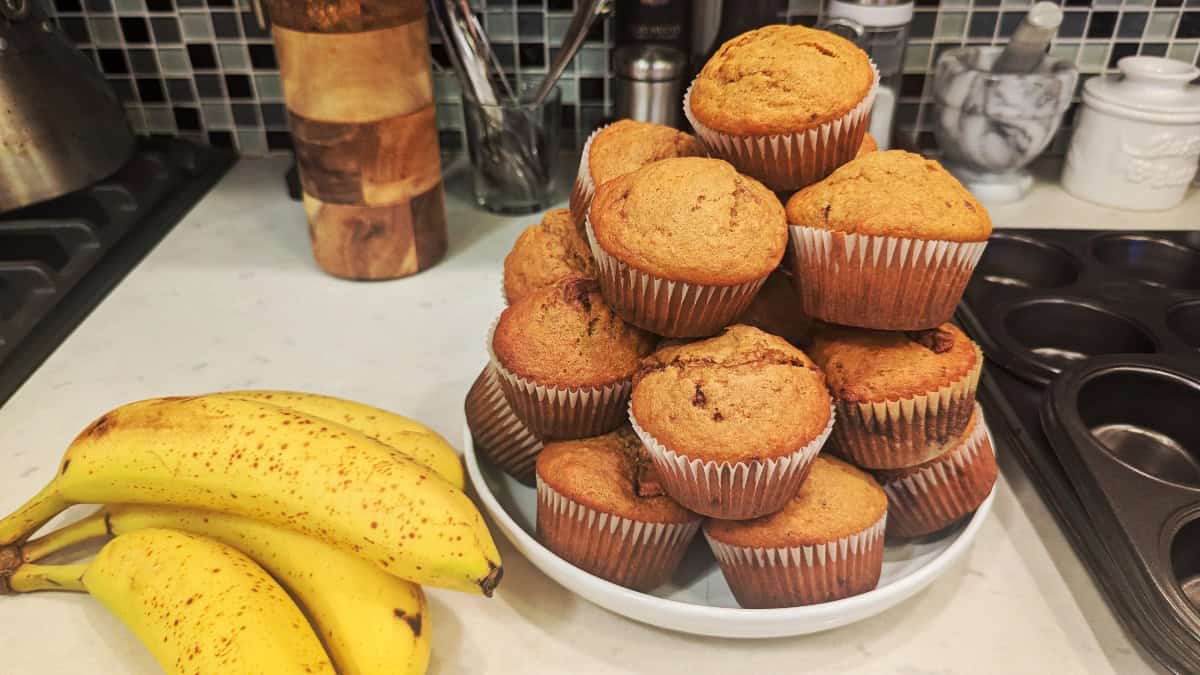Reese's Peanut Butter Cup Banana Muffins piled on a plate, next to a bunch of ripe bananas.