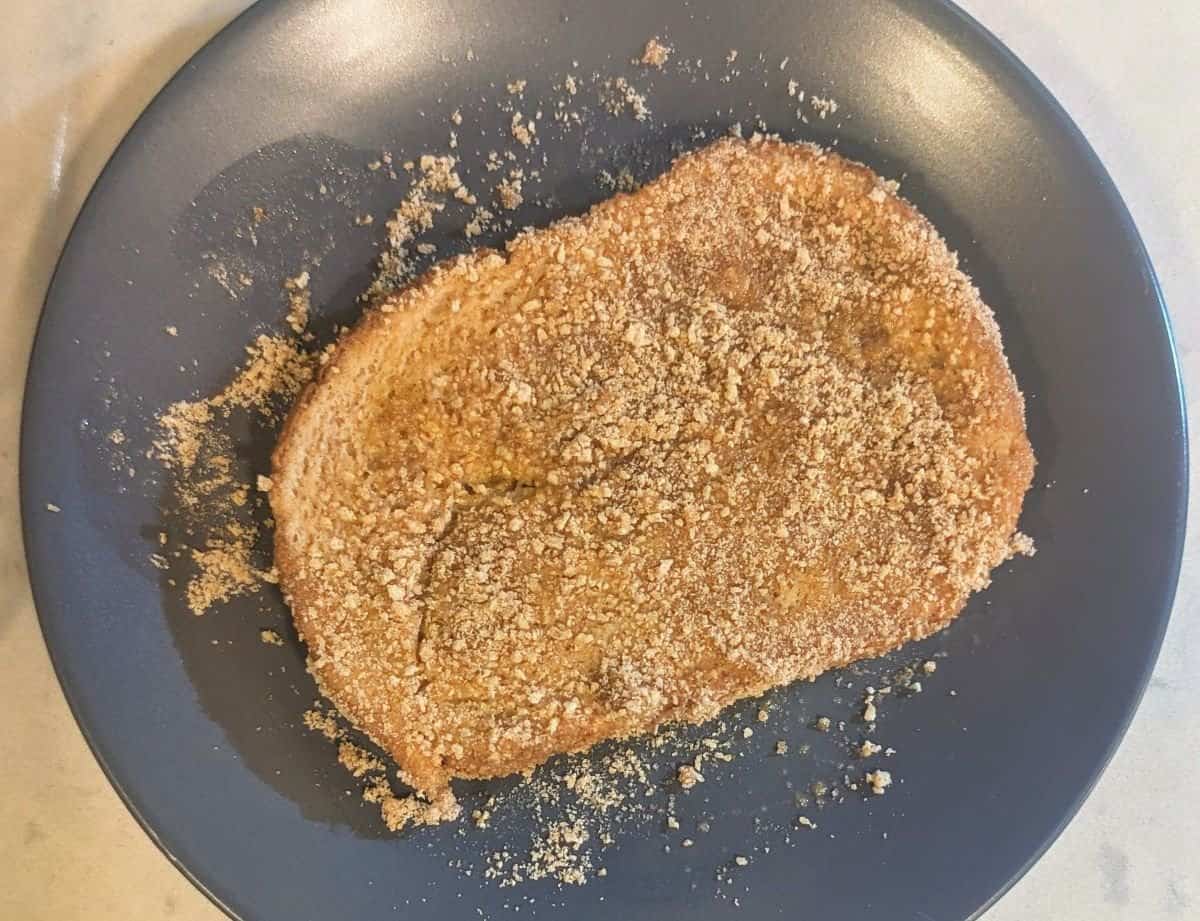 An uncooked piece of French toast covered in Cinnamon Toast Crunch crumbs.