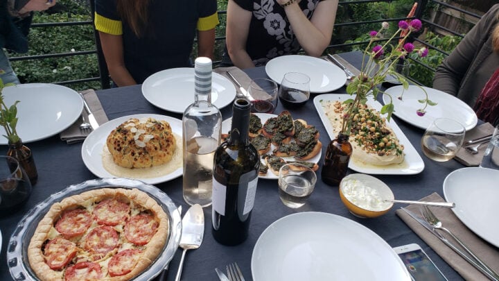 A table outdoors set with plates, wine, and food.