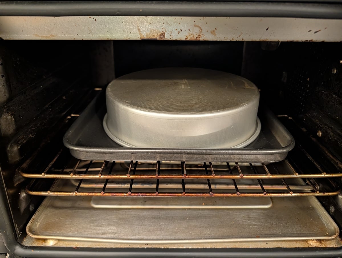 A square baking sheet and an inverted round cake pan in a toaster oven.